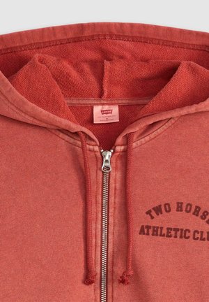 Rode zip-up hoodie met een gestructureerde afwerking, voorzien van een logo-opdruk "TWO HORSES ATHLETIC CLUB" en een metalen ritssluiting. Relaxte pasvorm, gevoerd met fleece.