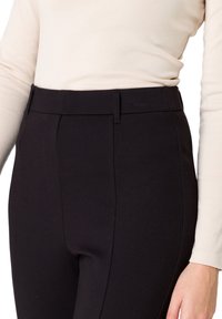 Pantalons noirs ajustés avec une texture lisse, présentant une coupe slim, une taille mi-haute et des détails de coutures subtils à l'avant.