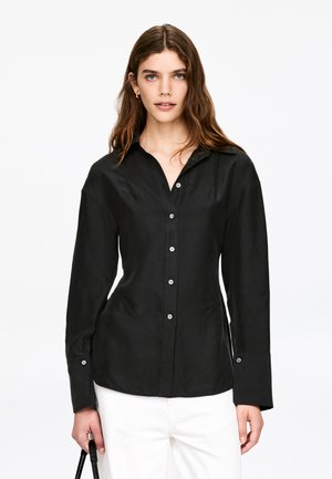 Zwarte longsleeve met knoopsluiting aan de voorkant, puntkraag en geribbelde manchetten. Gemaakt van gladde stof met een aansluitend ontwerp.