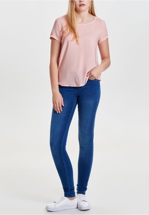 Hellrosa kurzärmliges Oberteil mit rundem Ausschnitt, kombiniert mit blauen Skinny-Jeans und weißen Sneakern, zeigt einen einfachen und lässigen Look.