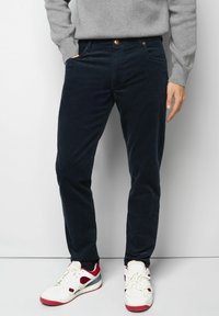 Marineblaue Cordhosen mit schmaler Passform, ausgestattet mit Seitentaschen und einem Knopfverschluss, kombiniert mit weißen und roten Sneakers.
