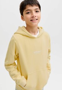 Sweat à capuche jaune en tissu doux, avec une poche avant, une capuche et le logo blanc "JJ Studios" imprimé sur la poitrine.