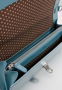 Blå läderhandväska med dragkedjestängning, med ett inre av brunt tyg med pricka och flera fack för organisering.