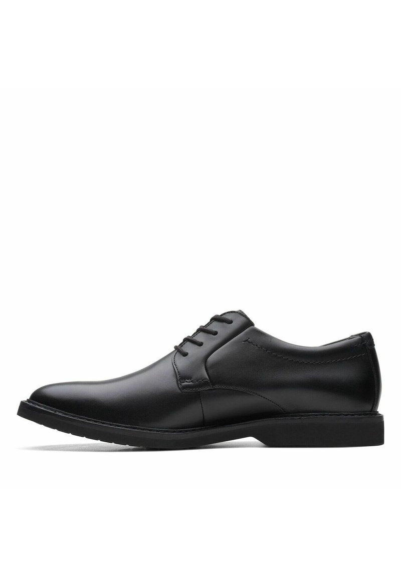 Zapato de vestir negro de cuero con textura suave, punta redonda y cinco ojales para cordones. Suela de goma negra de perfil bajo con detalles de costura sutiles.