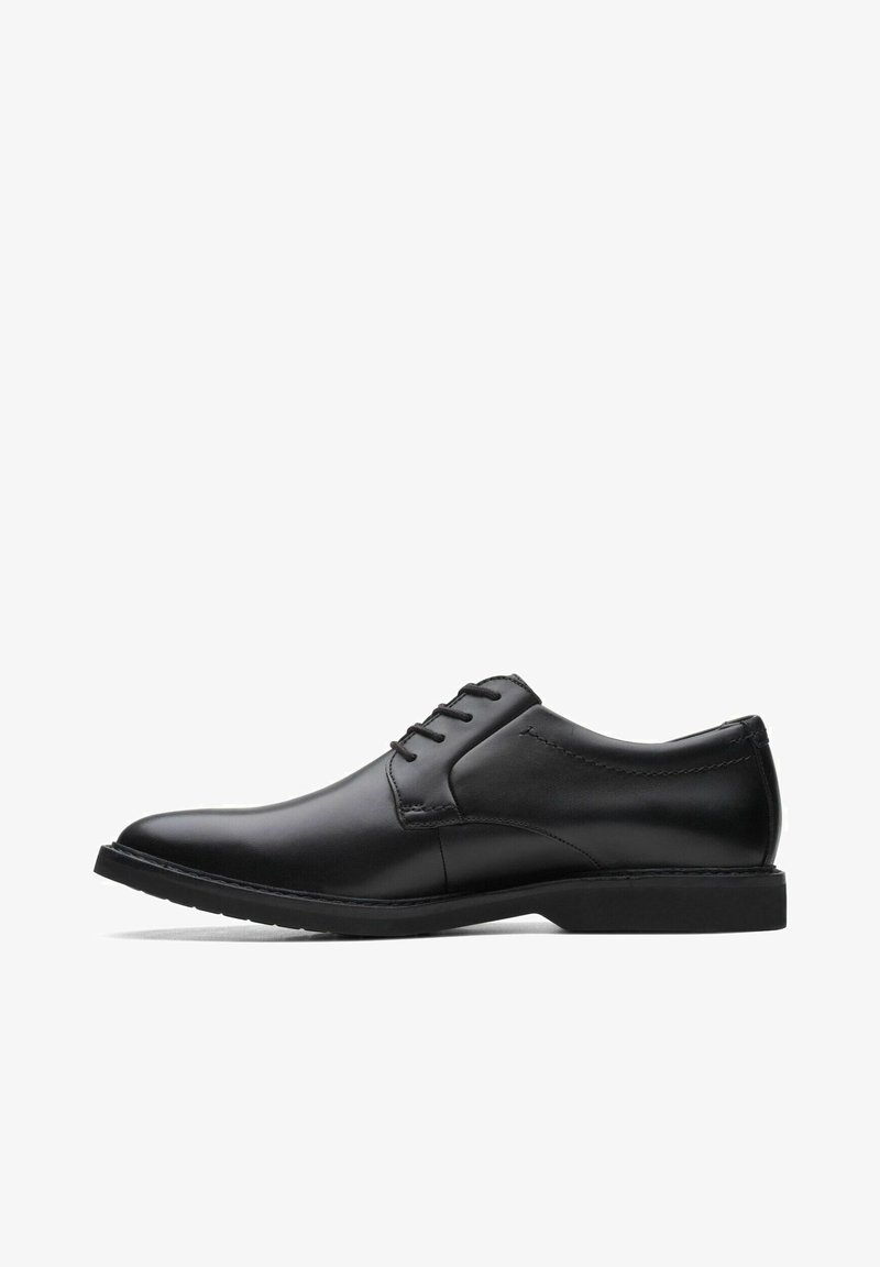 Zapato de vestir negro de cuero con textura suave, punta redonda y cinco ojales para cordones. Suela de goma negra de perfil bajo con detalles de costura sutiles.
