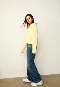 Pull jaune raccourci avec ourlet côtelé et manches longues ; associé à un jean bleu taille haute à jambes larges et des baskets blanches.