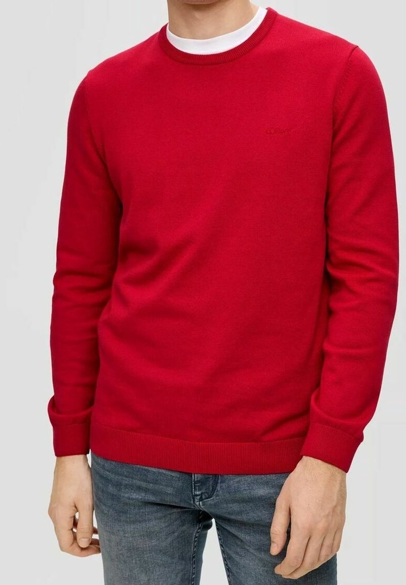 Rode gebreide trui met een ronde hals, geribbelde manchetten en onderrand. Bevat een subtiele logo op de borst. Gecombineerd met blauwe denim jeans.