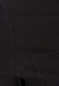 Černá tkanina s měkkou texturou, která má viditelné stehy a švy, ukazuje detailní pohled na hladký povrch materiálu.