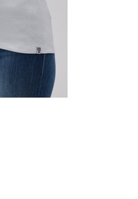 White ribbed t-shirt with a rounded hemline. Tag visible at the bottom left. Paired with dark blue denim jeans in a close-up view.