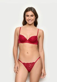 Conjunto de sujetador y braga de encaje rojo que presenta copas acolchadas, tirantes finos y bordes ondulados, mostrando un patrón floral sobre un fondo satinado.