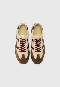 Adidași din piele bej cu accente marsala și vârf din suede maro. Au șireturi rotunde și detaliu negru pe călcâi. Design minimalist.