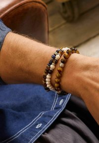 Bracciali di perle con tonalità marroni, blu e bianche, caratterizzati da diverse texture e materiali, con una combinazione di perle lisce e lucide.