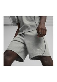 Graue Sportshorts aus weichem Material, mit einem kontrastierenden dunklen Naht, Logo am linken Bein und einem verstellbaren Bund.