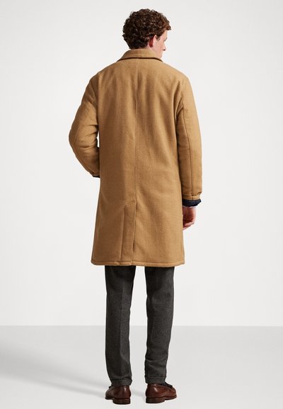 Bruine wollen jas met een gestructureerde silhouet, voorzien van een klassieke kraag, lange mouwen en een vent aan de achterkant, gecombineerd met grijze broek.