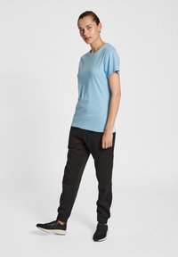 Ljusblå t-shirt med kort ärm och rund hals, kombinerad med svarta joggare. Modellen bär svarta sportskor och står på en neutral bakgrund.