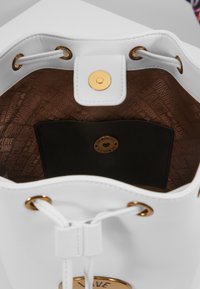 Vitt läderhinkväska med guldaccenter, brun innervägg tryckt med "Love Moschino" och svart innerficka med en knapp med guld-logotyp.