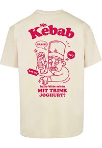 Kremo spalvos marškinėliai su pieštuku nupieštu šefu, laikydami kebabą, raudonu tekstu, kuriame yra "Mr. Kebab" ir kalbėjimo burbulu, sakant "HABIBI."