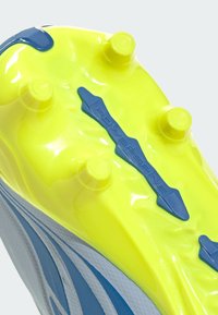 Semelle crantée jaune et bleue d'une chaussure de sport avec six crampons ronds et une bande centrale bleue de soutien "PowerSpine".