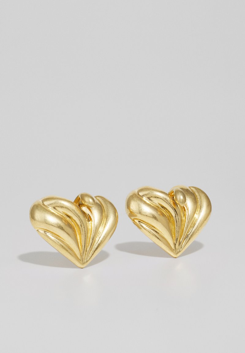 Χρυσά σκουλαρίκια σε σχήμα καρδιάς με υφή που διαθέτει καμπύλες αυλακώσεις και λείο χαρακτηριστικό στο κέντρο. Γυαλιστερή φινίρισμα.