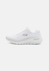 Zapatilla deportiva blanca con una parte superior de malla transpirable, superficie texturizada, acentos plateados, diseño de cordones y una suela acolchada.
