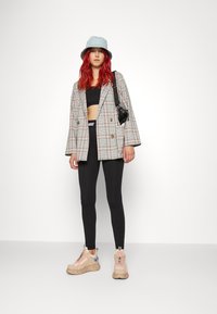 Sacou oversized din material în carouri, top cropt negru, colanți negri și pantofi sport bej cu talpă groasă. Pălărie din denim bleu deschis și geantă mică neagră tip crossbody.