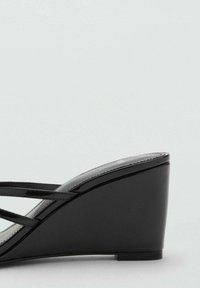 Sandalias cuña negras con un acabado de charol brillante, que presentan tiras entrelazadas y una banda suave en la parte delantera. Tacón corto y suela resistente.
