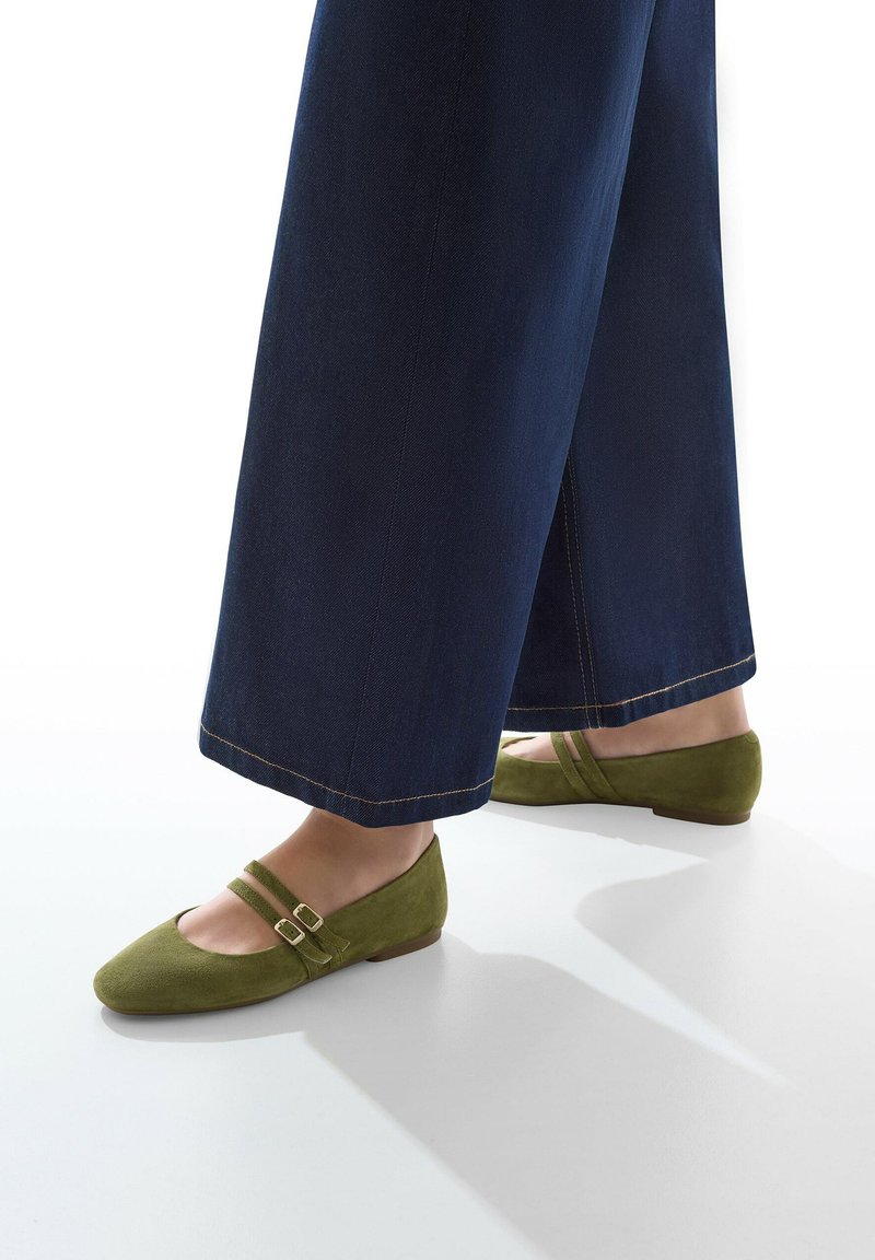 Ballerines en daim vert avec deux fines brides et des boucles dorées. Associées à un pantalon en denim bleu foncé à jambes larges. Texture lisse, design à bout arrondi.