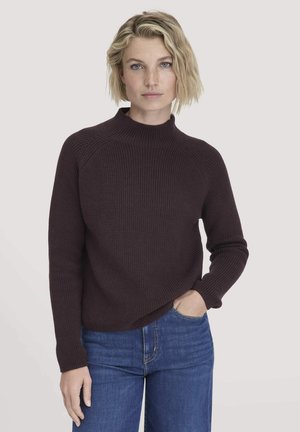 Bordeauxrot gerippter Strickpullover mit hohem Kragen und Raglanärmeln, kombiniert mit blauen Jeans. Die Textur wirkt weich und warm.
