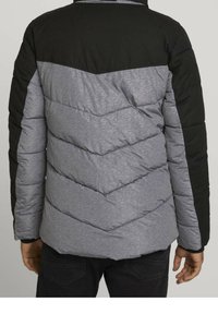 Veste rembourrée avec une partie supérieure noire et une partie inférieure grise avec un matelassage en chevrons. Le matériau semble lisse avec un léger éclat.
