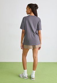 Grå bomulls T-skjorte med korte ermer og avslappet passform, paret med lyse beige shorts. Modellen har på seg hvite og sølv atletiske sko.