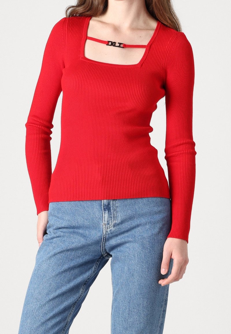 Haut rouge à manches longues côtelé avec un col carré et une bretelle d'accent noire. Associé à un jean en denim bleu clair.