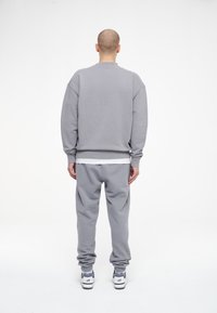 Completo in felpa grigia composto da felpa e pantaloni della tuta, caratterizzato da una vestibilità comoda, polsini a coste e un tessuto morbido e texturizzato. Abbinato a sneakers bianche e grigie.