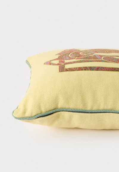 Coussin en tissu jaune avec un motif cachemire multicolore et un passepoil vert le long des bords sur fond blanc.