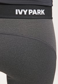 Svarta träningsleggings med en åtsittande design, som har en bred midjeresår märkt "IVY PARK" i vit text. Slät, elastisk tyg med en subtil textur.