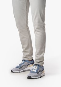 Blaue und graue SportSneaker aus Mesh- und Wildledermaterialien, mit Schnürverschluss und einer klobigen weißen Sohle, kombiniert mit hellgrauen Slim-Fit-Hosen.