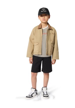 Veste beige clair avec col marron, t-shirt rayé, short noir et baskets montantes avec lacets blancs. Design simple et décontracté.