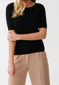 Top in maglia a coste nera con scollo rotondo e maniche corte, abbinato a pantaloni beige sartoriali. Texture liscia e design aderente.