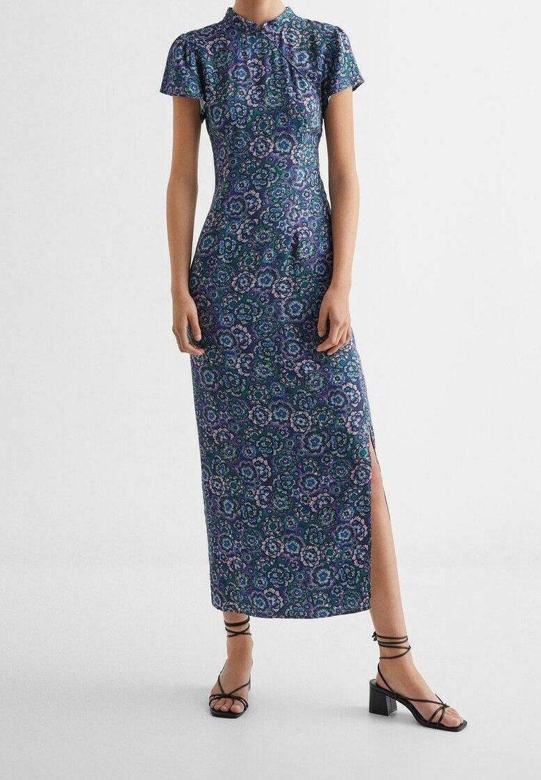 Šaty s přiléhavým střihem, krátkým rukávem a vysokým límečkem, zdobené modrým květinovým vzorem, s bočním rozparkem a spárovány s černými sandály na pásky.