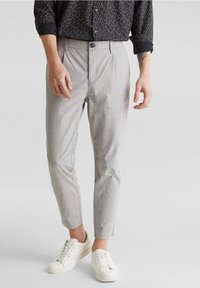Šedé kostkované kalhoty slim fit, vyrobené z lehkého materiálu. Mají zapínání na knoflík a boční kapsy. Kombinované s bílými teniskami.