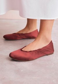 Scarpe flat in un ricco tessuto bordeaux presentano una punta rotonda e un'apertura elasticizzata, esposte su una superficie leggera e strutturata.