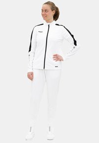 Weißes sportliches Trainingsanzug mit schwarzen Akzenten und Branding. Besteht aus einer Jacke mit Reißverschluss und passenden Hosen, gefertigt aus einem glatten, leichten Material.