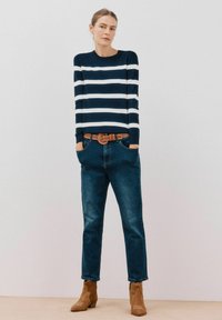 Maglione lavorato a maglia a righe navy e bianche, vestibilità comoda, abbinato a jeans denim scuri e una cintura marrone. Stivali alla caviglia marroni completano l'outfit.