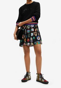 Pullover nero con strisce colorate ai polsini, abbinato a una gonna nera al ginocchio con disegni a patch multicolore e sneakers con motivo.