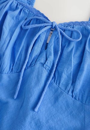 Blå stof top med snørebåndslukning foran, samlet talje og blonder kanter langs udskæringen. Blødt, tekstureret materiale.