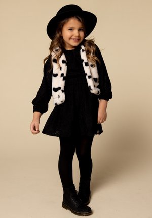 Zwarte kanten jurk met pofmouwen, gecombineerd met een witte fuzzy sjaal met zwarte harten; zwarte leggings en combatboots maken de outfit compleet.