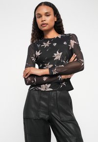 Top de malla negra de manga larga con un patrón floral en tonos de rosa y blanco; combinado con pantalones de cuero negros. Textura de tejido suave, diseño ajustado.