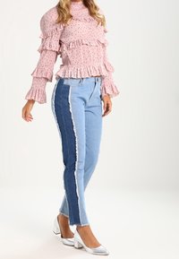 Růžový top s volány a dlouhými rukávy pokrytý puntíky, v kombinaci s dvoubarevnými džíny s třepením na bočním švu; modelka v stříbrných lodičkách na blokovém podpatku.