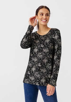 Langärmliges schwarzes Oberteil mit weißem und goldfarbenem Blumenmuster, rundem Ausschnitt, weichem Stoff und lockerer Passform. Getragen mit blauen Jeans.