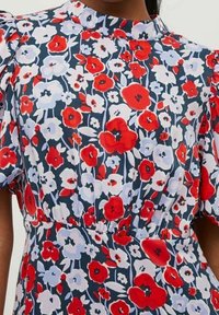 Robe fleurie avec un fond sombre orné de fleurs rouges et blanches, manches courtes bouffantes, col montant et taille froncée.