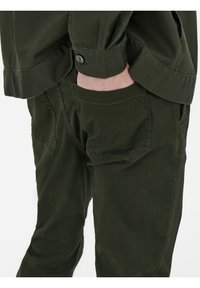 Olijfgroene katoenen shirt met een ontspannen pasvorm. Beschikt over knoopmanchetten en een borstzak. Glad textuur en subtiele stikdetails.